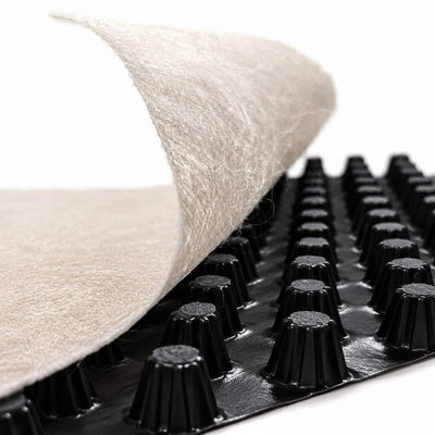 Close-up of a black drainage membrane with raised conical studs, showing a light beige fibrous filter layer being peeled back from one side against a white background.